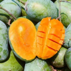 Mango with a half-cut section surrounded by whole green mangoes